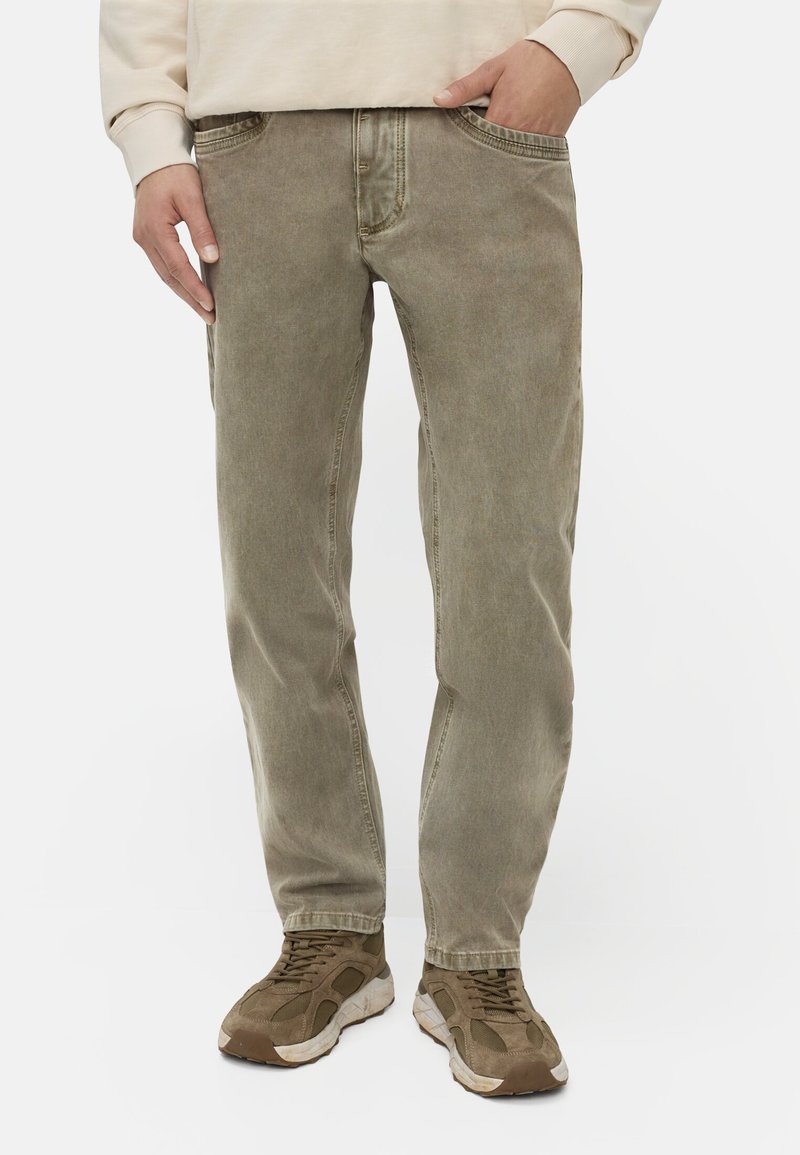 Olivengroene denim jeans met een recht model, vijf zakken en subtiele vervaging. Draagt bij bruine sneakers.