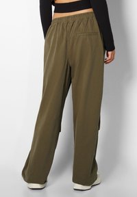 Pantaloni a palazzo verde oliva con vita elastica, dotati di spacchi laterali e una tasca sul retro, realizzati in tessuto morbido e cadente.