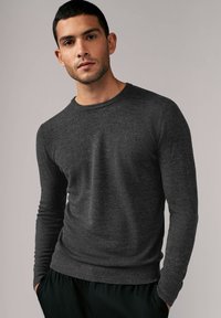 Dunkelgrauer Langarmpullover aus Strickstoff mit Rundhalsausschnitt, der eine dezente Textur und slim fit aufweist. Kombiniert mit schwarzen Hosen.