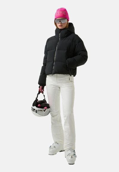 Zwarte donsjas, witte broek, roze gebreide muts met de tekst "FIRE", zonnebril en een helm met handschoenen erbij. Ski'schoenen zijn wit met zilveren accenten.