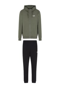 Felpa con zip verde oliva, dotata di coulisse e logo sul petto, abbinata a pantaloni joggers neri con elastico in vita, caratterizzati da un piccolo logo.