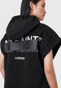 Svart oversized hoodie med huva, med vit text, en blank svart rand och "LONDON" tryckt vid fållen. Mjuk tygstruktur.