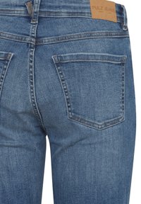 Modre jeans iz denima imajo gladko teksturo, pet žepov in svetlo rjav usnjen znak na zadnjem pasu s štampiljko "PULZ JEANS".