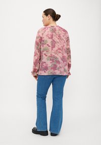 Blusa leggera a fantasia rosa con design floreale, maniche lunghe, dettaglio arricciato sulla schiena, abbinata a jeans a zampa blu e scarpe con plateau nere.