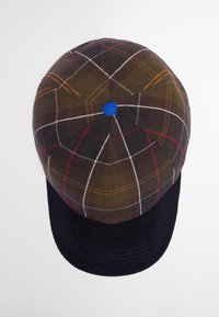 Καπέλο από καρό ύφασμα σε σκούρο πράσινο, κόκκινο και λευκό, με μπλε κουμπί στην κορυφή. Διαθέτει βραχίονα από ναυτικό κοτλέ και δομημένο σχήμα.