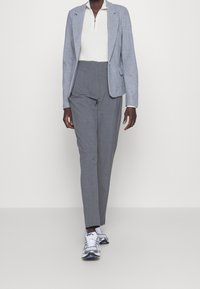Lichtblauwe blazer, witte geribbelde zip-top, grijze op maat gemaakte broek en witte/grijze sneakers. Glad materiaal, gestructureerde pasvorm, minimalistisch ontwerp.