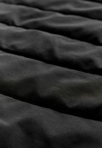 Gros plan sur un tissu matelassé noir doux avec des lignes cousues horizontales créant des sections rembourrées.