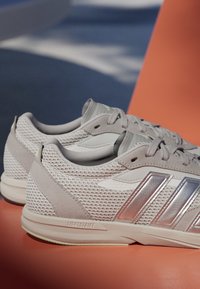 Světle šedé sportovní boty s koženými a semišovými panely, metalickými akcenty a silnou podrážkou s označením "LIGHTSTRIKE".