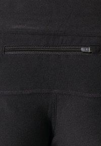 Czarne legginsy sportowe mają gładką fakturę, bezpieczną kieszeń na zamek z tyłu oraz wzmocnione szwy dla trwałości.