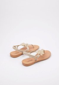 Chanclas beige con un acento de flor texturizada, que cuentan con una correa flexible y una suela de goma marrón. La marca es visible en la plantilla.