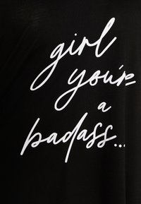Svart bomull t-shirt med vit kursiv text som säger "tjej, du är en badass..." med avslappnad passform och mjuk textur.