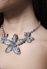 Sølv blomsterhalskæde med indviklet detaljer, der har tre teksturerede blomsterformer og klare rhinestone-henvisninger på en sølvkæde.