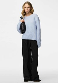 Pull en maille bleu clair à coupe décontractée avec des poignets côtelés, associé à un pantalon large à fines rayures noires et un sac noir texturé.