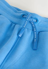 Zbliżenie na niebieski pas od spodni dresowych z bawełny z dopasowanym sznurowadłem z logo "Ted Baker" na sznurku i przelotkach.