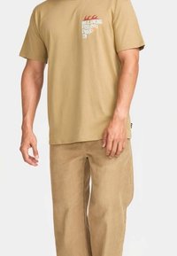 Beige katoenen t-shirt met korte mouwen en een grafische zak. Gecombineerd met beige corduroy broek, rechtvallende pasvorm en textielstructuur.