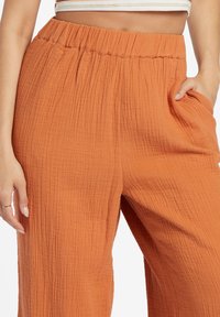 Orange crinkled wide-leg pants with an elastic waistband and side pockets. The fabric has a textured appearance.