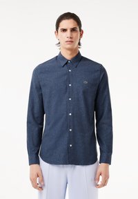 Camisa abotonada azul oscuro hecha de una tela texturizada, con cuello puntiagudo y un pequeño logo verde en el lado izquierdo del pecho.