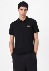Zwarte polo shirt in katoenmix, met een twee-knopen knoopsluiting en een gouden logo op de linkerkant van de borst. Korte mouwen en een klassiek kraagontwerp.