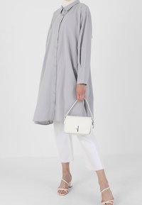 Robe chemise oversize gris clair avec des boutons, des manches longues et un col. Associée à un pantalon cropped blanc et un sac à main matelassé blanc.