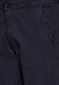 Námorně modré látkové kalhoty s hladkým povrchem, s knoflíkovým zapínáním a bočními kapsami, s podrobným švem podél švů.