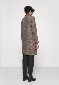 Abrigo largo rosa con manchas negras, con cuello y corte recto, llevado sobre pantalones de cuero negros y botines de tacón.