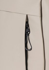 Lichtbeige tas met een gestructureerde oppervlakte, zwarte ritsdetails en een treklipje. Het ontwerp is strak met gestructureerde naden.