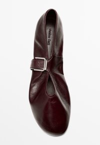 Bordeauxrode leren schoen met een afgeronde neus, uitsnijdingen en een zilveren gespsluiting aan de zijkant. Gladde textuur en minimalistische stijl.