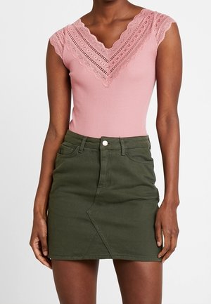 Roze ribgebreide body met kanten rand en een V-hals, gecombineerd met een groene denim minirok met een asymmetrische zoom en een voorsluitingsknopen.