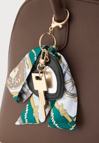 Καφέ δερμάτινη τσάντα με χρυσά μεταλλικά στοιχεία, που διαθέτει μπρελόκ στολισμένο με πολύχρωμο μεταξωτό φουλάρι και μαύρο δακτύλιο για κλειδιά.