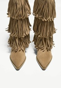 Brązowe zamszowe botki za kostkę z warstwowym frędzlowaniem, spiczastymi czubkami i fakturowanymi powierzchniami. Charakteryzują się subtelnym, kontrastującym obcasem.
