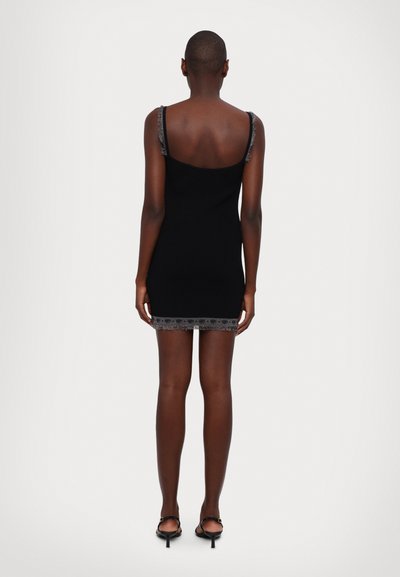 Robe en tricot noire à fines bretelles, avec une dentelle au niveau de l'ourlet. Le dos est lisse avec un design ouvert, mettant en valeur une silhouette ajustée.