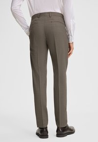 Brązowe wzorzyste spodnie o dopasowanym kroju, z dwoma tylnymi kieszeniami i wyprasowanymi kantami, w połączeniu z czarnymi butami.