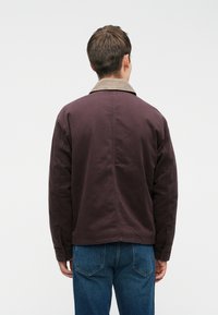 Brun bomuldsjakke med et kordfløjlskrage, der har en afslappet pasform og enkle stikdetailler, parret med blå denimjeans.