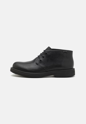 Black leather ankle boots with a rounded toe, lace-up design, and a rubber sole. Features a smooth texture and a minimalist style.