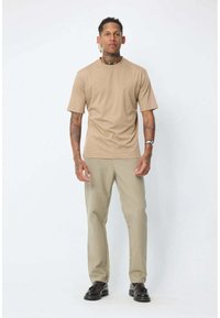 T-shirt beige à manches courtes associé à un pantalon beige clair. Le tissu semble lisse, avec une coupe décontractée et un col rond. Des chaussures noires complètent le look.