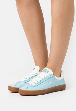Light blue suede sneakers with white laces and accents. Features a tan rubber sole and a logo on the tongue. Smooth texture overall.