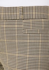 Brun och vit houndstooth-mönstrad tyg med en slät textur; har en bakficka och en platt midjebandsdesign.