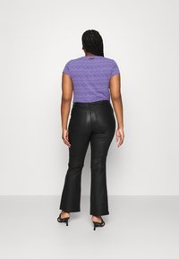 T-shirt violet à motifs avec des manches courtes associé à un pantalon évasé noir. La tenue présente une silhouette ajustée et des textures lisses.
