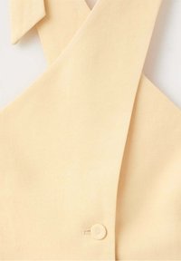 Gros plan sur une cravate en tissu beige attachée par un petit bouton rond sur un vêtement.