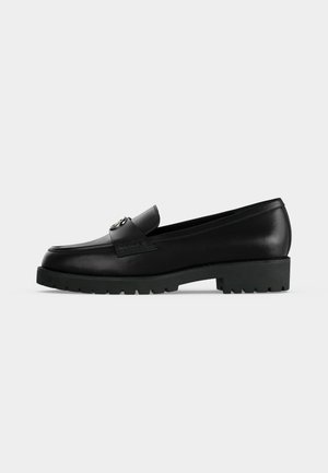Mocassin femme en cuir noir avec semelle épaisse et détail boucle métallique sur le dessus, présenté en profil latéral sur fond blanc.