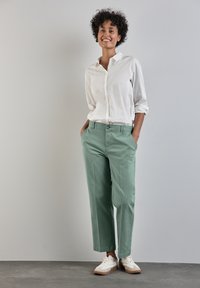 Chemise blanche à boutons portée avec un chinos vert clair. Tissu doux, coupe décontractée, jambes droites et poches latérales. Assortie à des baskets blanches.