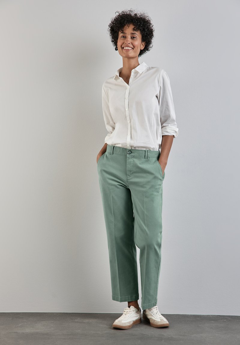 Chemise blanche à boutons portée avec un chinos vert clair. Tissu doux, coupe décontractée, jambes droites et poches latérales. Assortie à des baskets blanches.