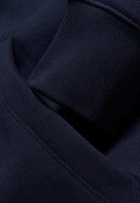 Tejido de sudadera de algodón de color azul marino con una superficie texturizada, que presenta un puño doblado y detalles de costura visibles.