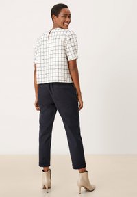 Haut à manches courtes à carreaux blancs avec un dos en fente, associé à un pantalon bleu marine fuselé et des bottines beiges à talon aiguille.