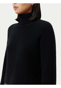 Svart ribbad polotröja med långa ärmar. Det texturerade tyget ger ett mysigt utseende. Halsringningen är åtsittande med en lätt stretch.