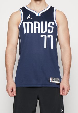 Homme portant un maillot de basketball Dallas Mavericks bleu foncé avec le numéro 77 et un short noir avec un logo Jumpman.