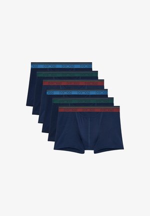 Hombre en forma de pie descalzo con calzoncillos bóxer azul oscuro sobre fondo claro y liso.