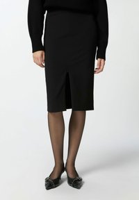 Crna olovka suknja s prednjim prorezom, napravljena od glatke tkanine. Uparena s prozirnim crnim čarapama i crnim štiklama s uskim vrhom s detaljima.