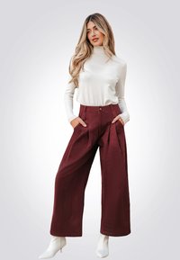 Bordeaux wijde broek met plooiingen, zijzakken en een knoopsluiting, gecombineerd met een strakke beige coltrui en witte enkellaarsjes.