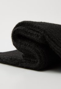 Coperta in lana nera lavorata a maglia, arrotolata con una superficie morbida e testurizzata. Presenta un motivo di maglia uniforme e un minimo sfilacciamento lungo i bordi.